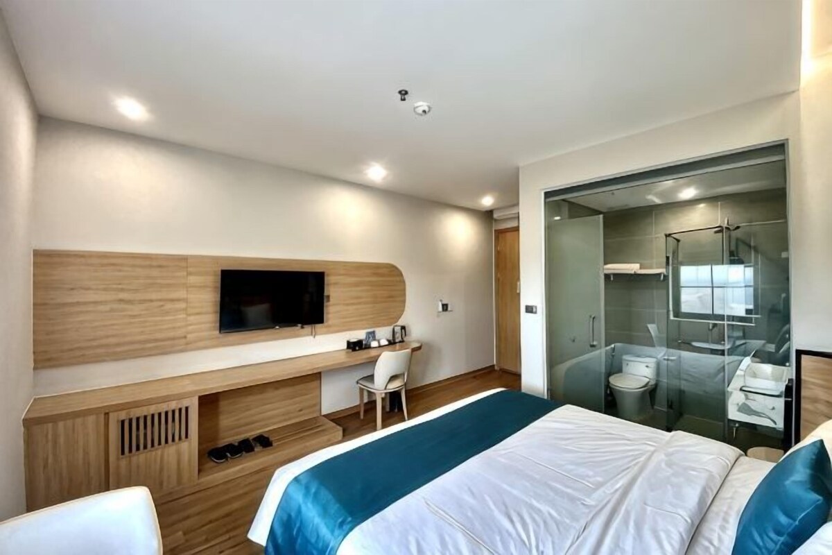 A modern hotel room with a bed, a desk, a TV, and a shower area.