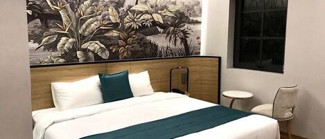 A hotel room with a large bed, a small round table, a chair, and a mural of a tropical scene on the wall.