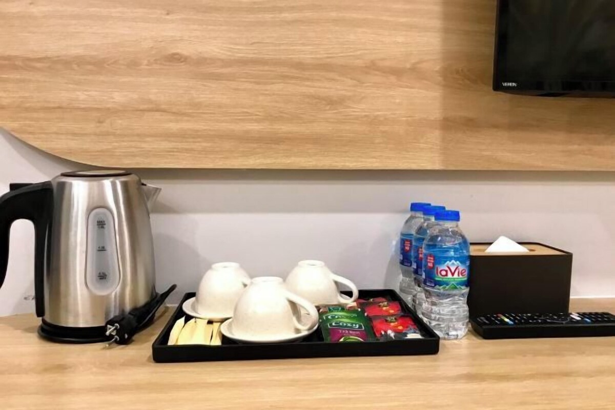 Une chambre d’hôtel avec un mur en bois, une bouilloire, des tasses à thé, un plateau avec des collations, des bouteilles d’eau et une télécommande.
