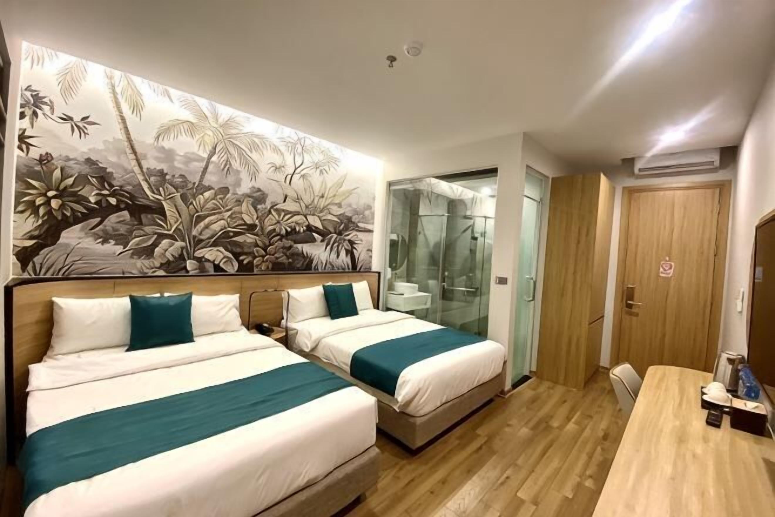 Habitació d'hotel amb dos llits, un sòl de fusta, un mural gran, zona de dutxa i una porta de fusta.