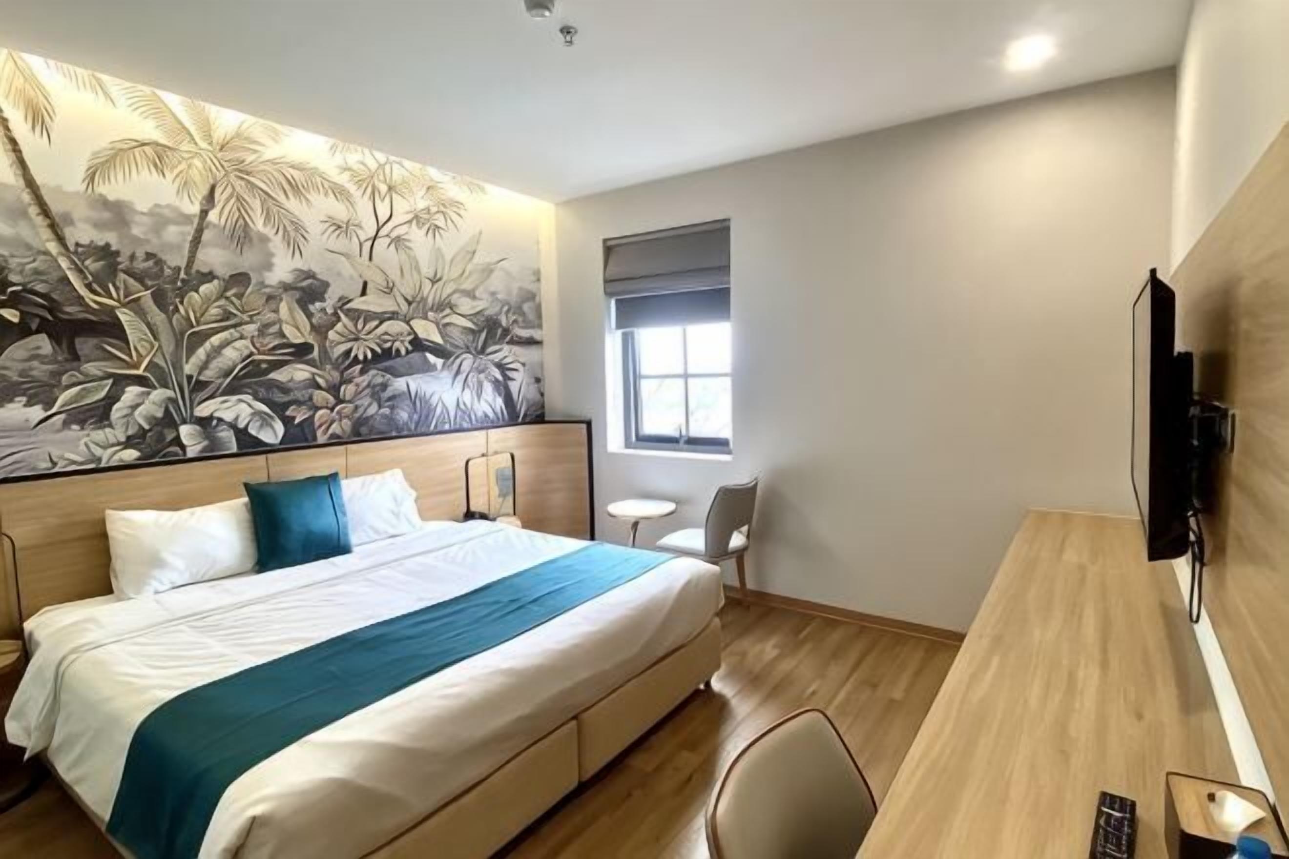 Habitació d'hotel amb llit, escriptori, cadira, televisió, finestra i mural a la paret.