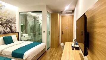 A hotel room with two beds, a TV, a desk, and a shower area.