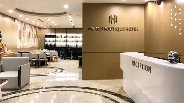 A modern hotel reception area with a reception desk labeled "RECEPTION" and a wall-mounted logo. - Milash Boutique Hotel (Bai Chay)