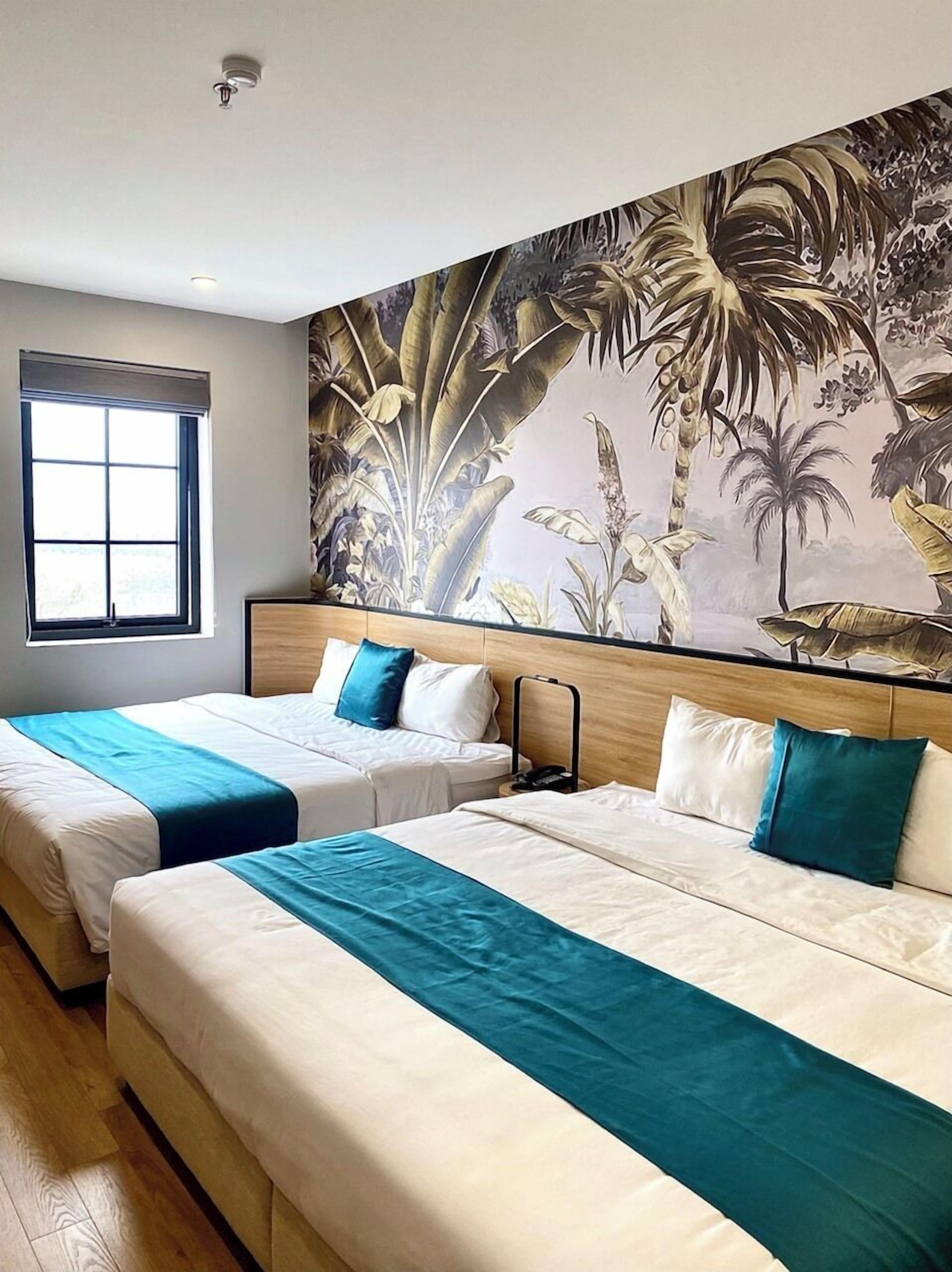 A hotel room with two beds, a large window, and a mural of tropical plants on the wall.