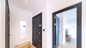A hallway with a bench, a door, and a view into another room with a lamp and a plant. - Bright and Quiet | Spacious Apt with Balcony and Lift (Greater London)