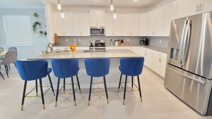 A modern kitchen with white cabinets, a stainless steel refrigerator, and blue bar stools.