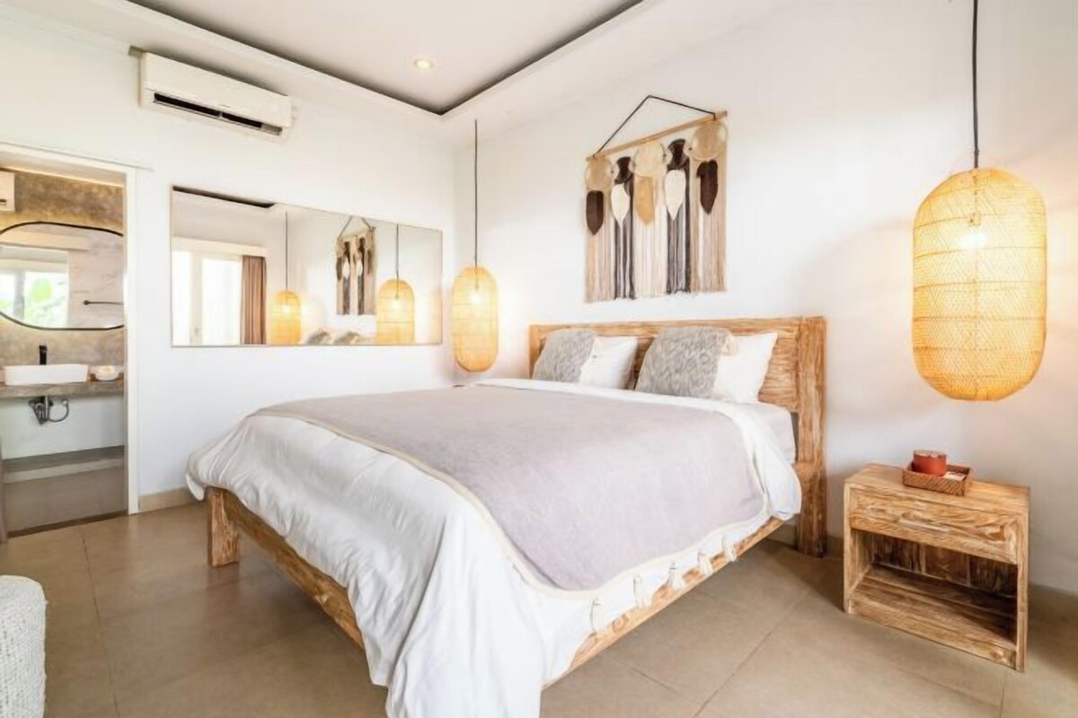 A bedroom with a wooden bed, a bedside table, a hanging light fixture, and a wall-mounted artwork.