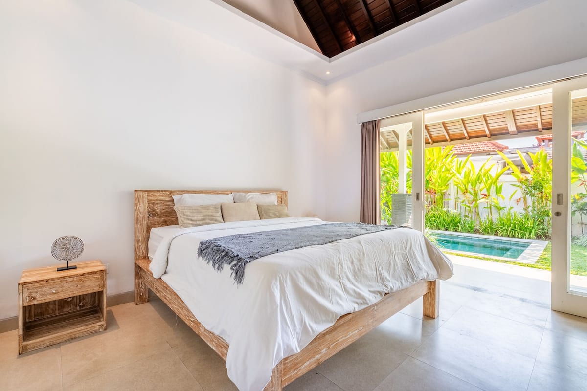 A bedroom with a wooden bed, a bedside table, and a view of a swimming pool.