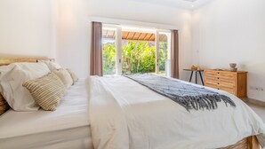 A bedroom with a bed, a wooden dresser, and a view of greenery outside. - Jungle Amaranth Villa Canggu - Exclusive 3BR Retreat with Pool, Modern Amenities and Top Location (Canggu)