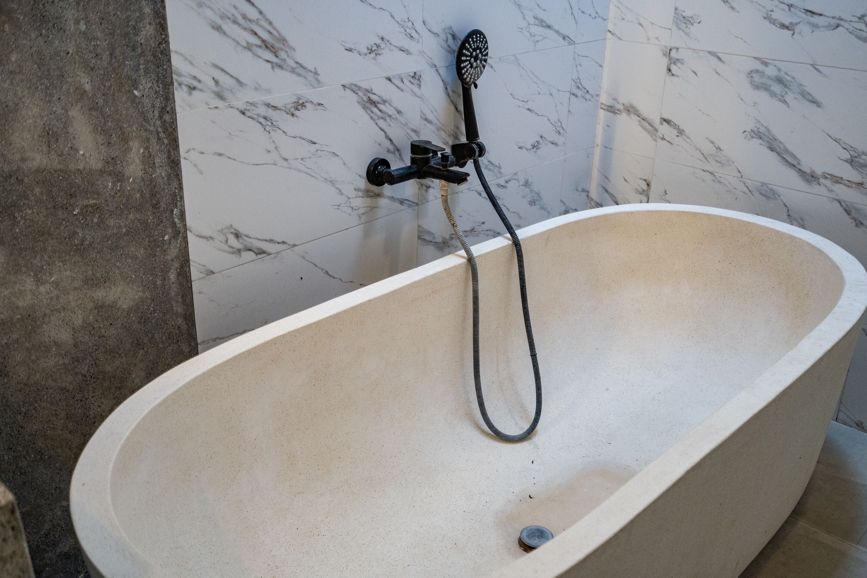 A bathtub with a handheld showerhead in a bathroom with marble walls.