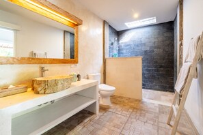 A bathroom with a stone sink, a white toilet, a shower area with a dark stone wall, and a wooden floor. - Jungle Amaranth Villa Canggu - Exclusive 3BR Retreat with Pool, Modern Amenities and Top Location (Canggu)