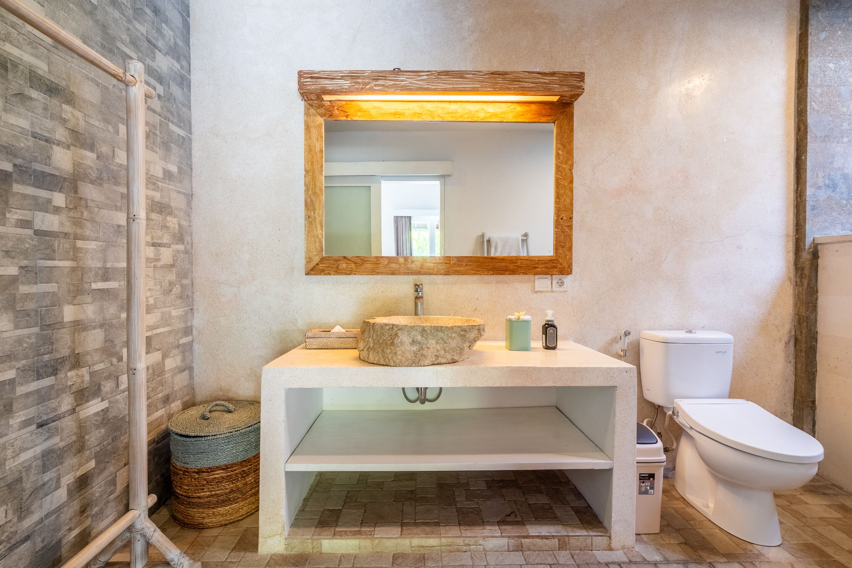 A bathroom with a stone sink, a wooden-framed mirror, a toilet, and a shower area.