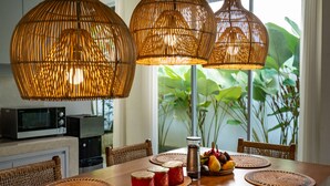A dining area with a wooden table, wicker chairs, and a view of greenery through a window. - Jungle Amaranth Villa Canggu - Exclusive 3BR Retreat with Pool, Modern Amenities and Top Location (Canggu)