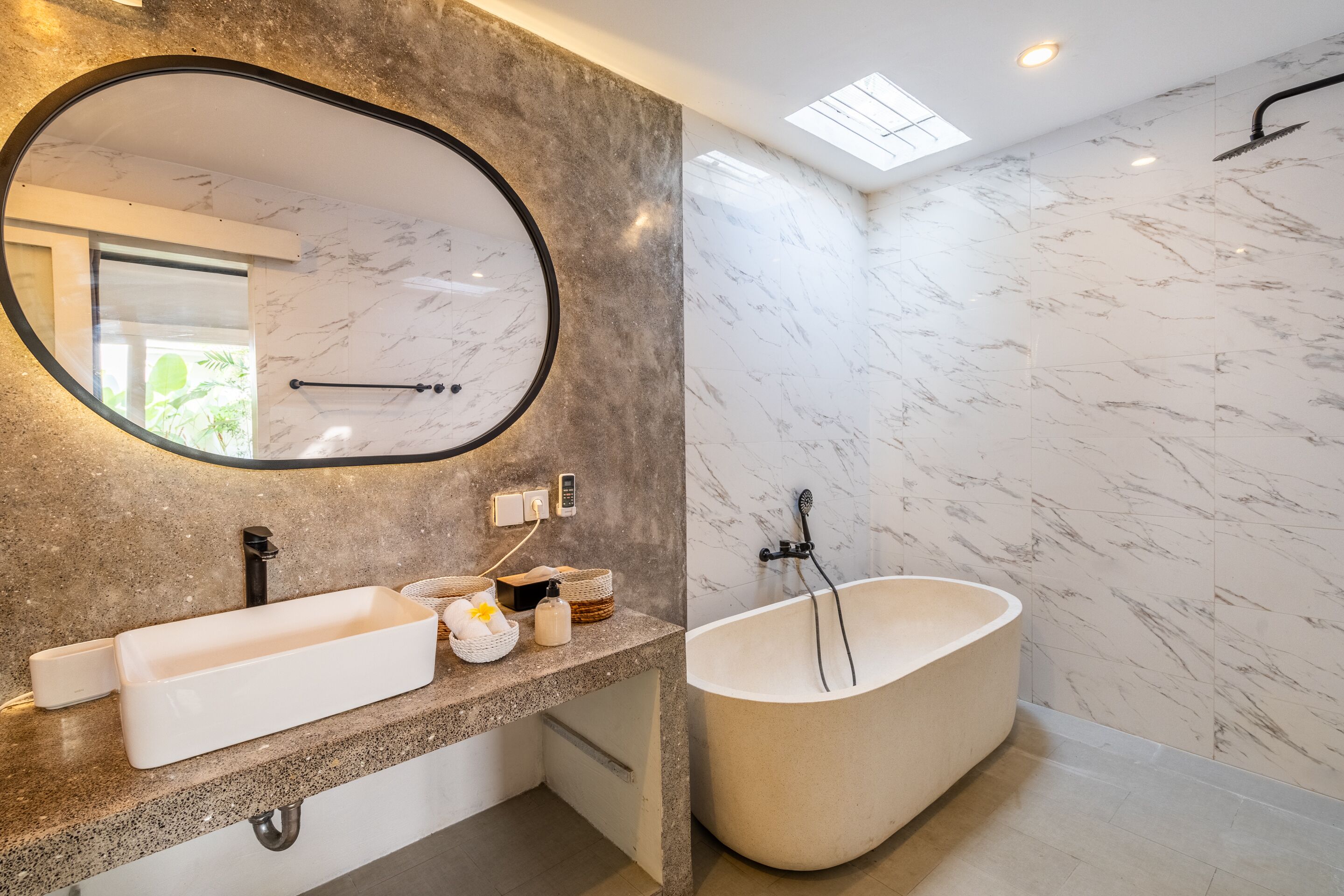 A modern bathroom with a freestanding bathtub, a large oval mirror, and a granite countertop.