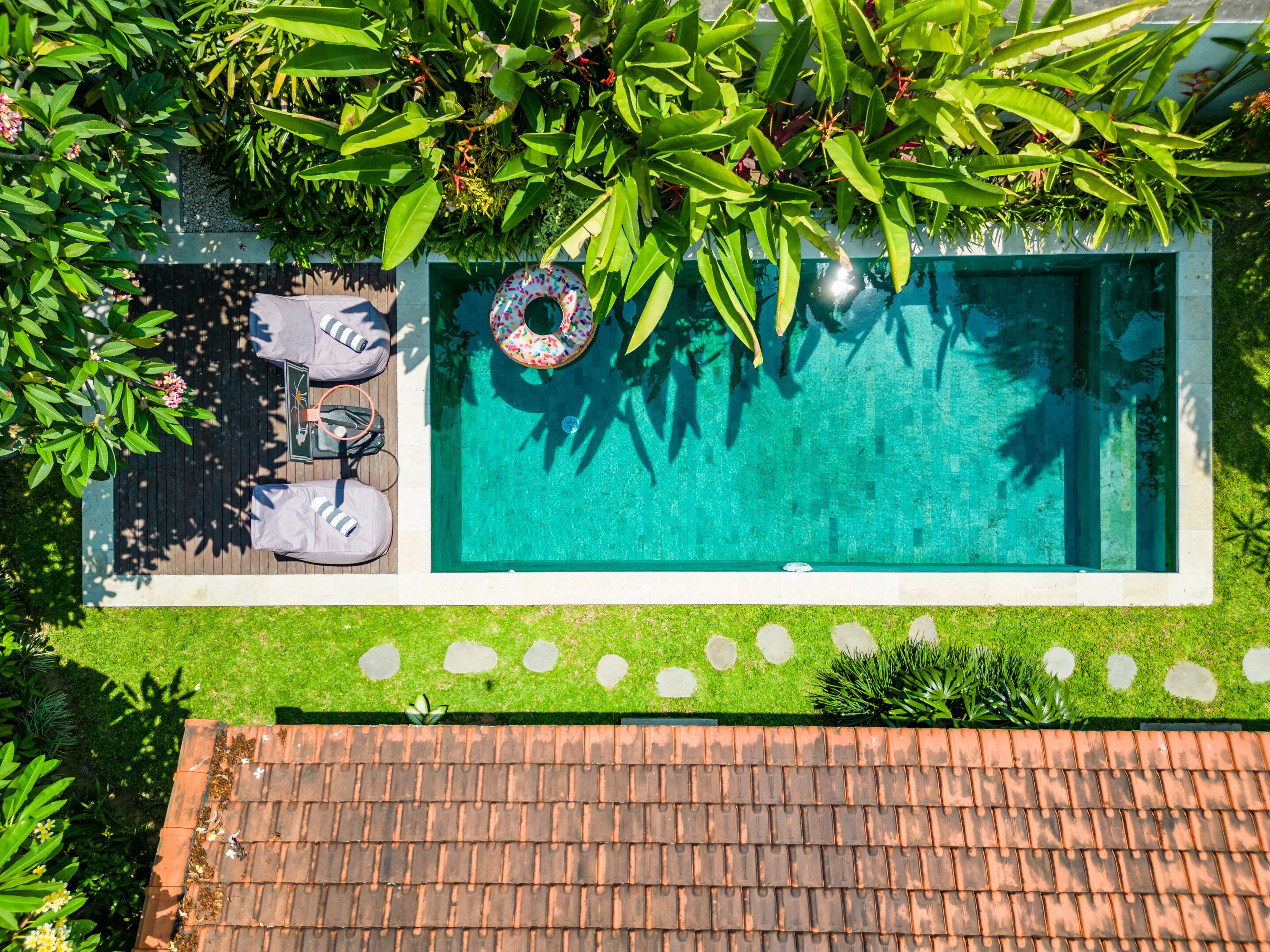 A rooftop pool with a clear blue water surface, surrounded by lush greenery and a wooden deck with lounge chairs and a barbecue grill.