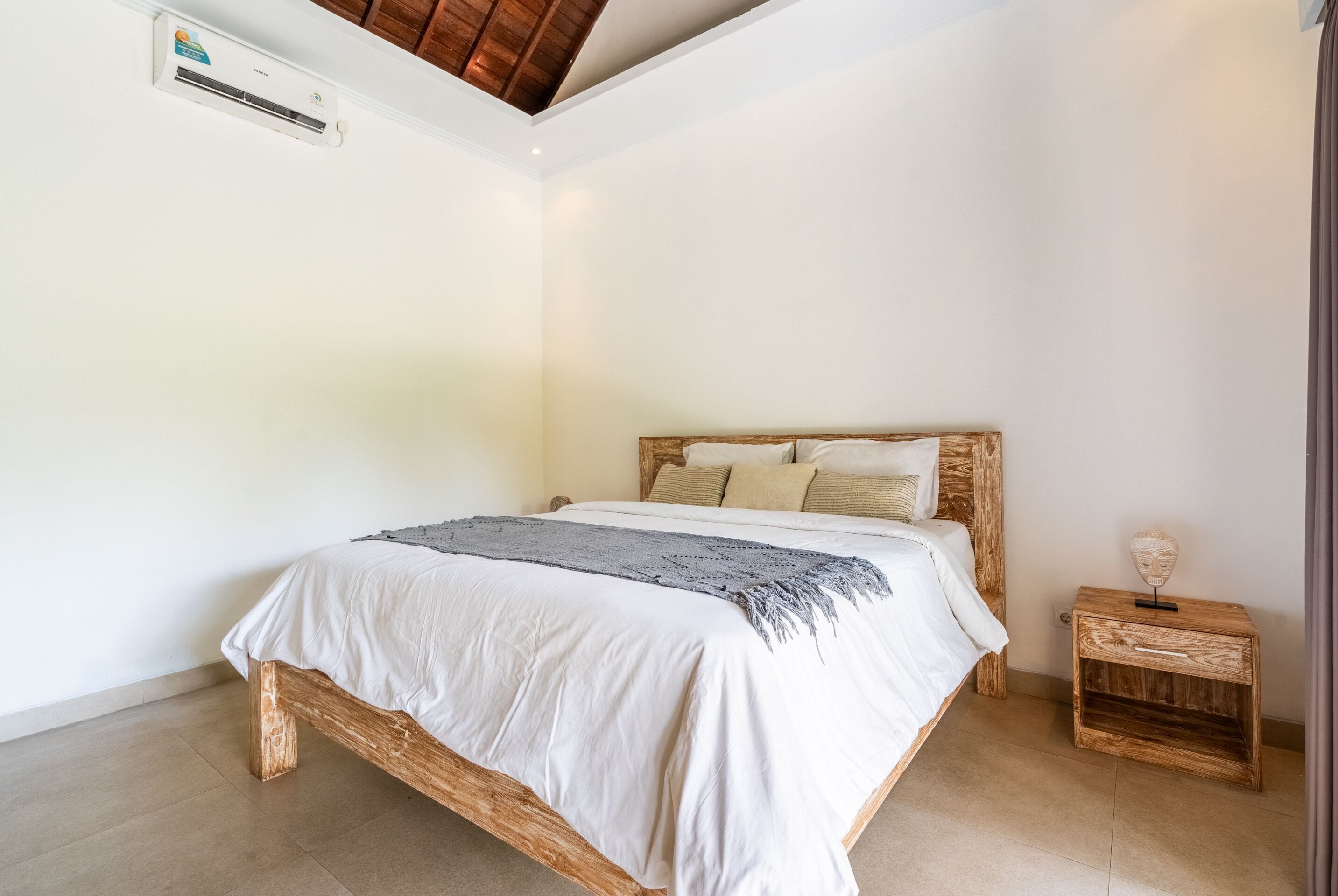 Une chambre à coucher avec un lit en bois, du linge de lit blanc, une petite table de chevet en bois et un ventilateur de plafond.