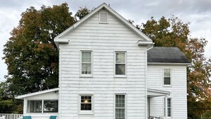 A white two-story house with a porch, a front yard, and a driveway.