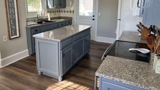 A kitchen with a central island, grey cabinets, a double door, and a refrigerator.