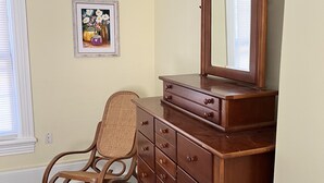 A room with a wooden dresser, a wicker chair, and a framed picture on the wall.