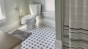 A bathroom with a toilet, a bidet, a shower curtain, and a window with blinds.