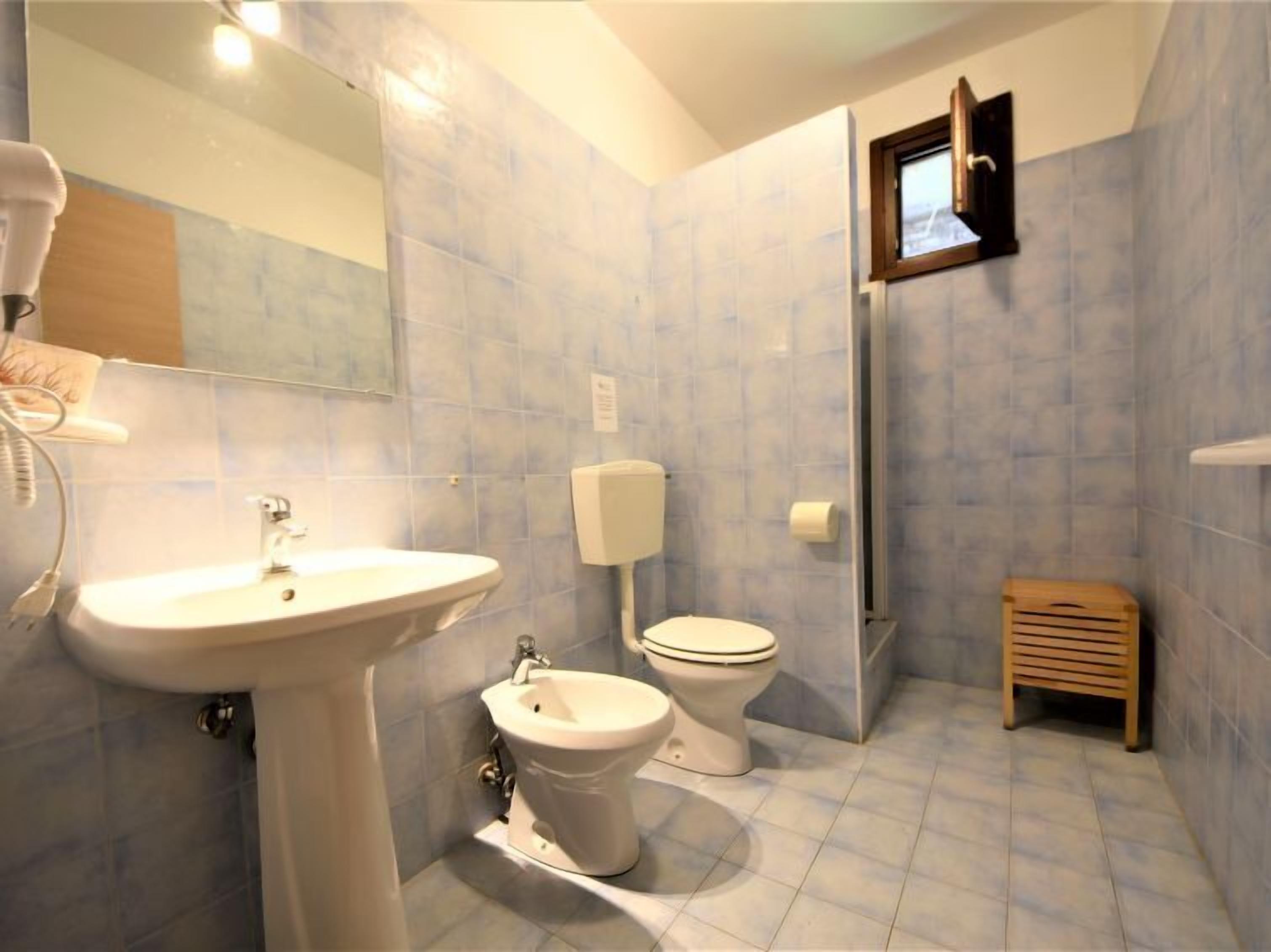Et badeværelse med et konsolbordvask, en bidet, et toilet og en lille træskammel.