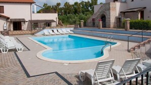 Ein Swimmingpool mit Liegestühlen, einer Steinmauer und einem Gebäude mit Ziegeldach.