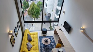 A modern apartment with a large window, a yellow sofa, a dining table, and a TV mounted on the wall. - Loft moderno con vista a los cerros  (Bogotá)
