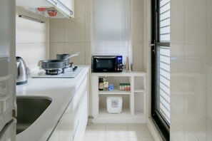 Een kleine keuken met een magnetron, fornuis en diverse keukengerei.