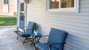 Une terrasse avec deux chaises bleues et une petite table, une plante en pot et une fenêtre donnant sur un immeuble.