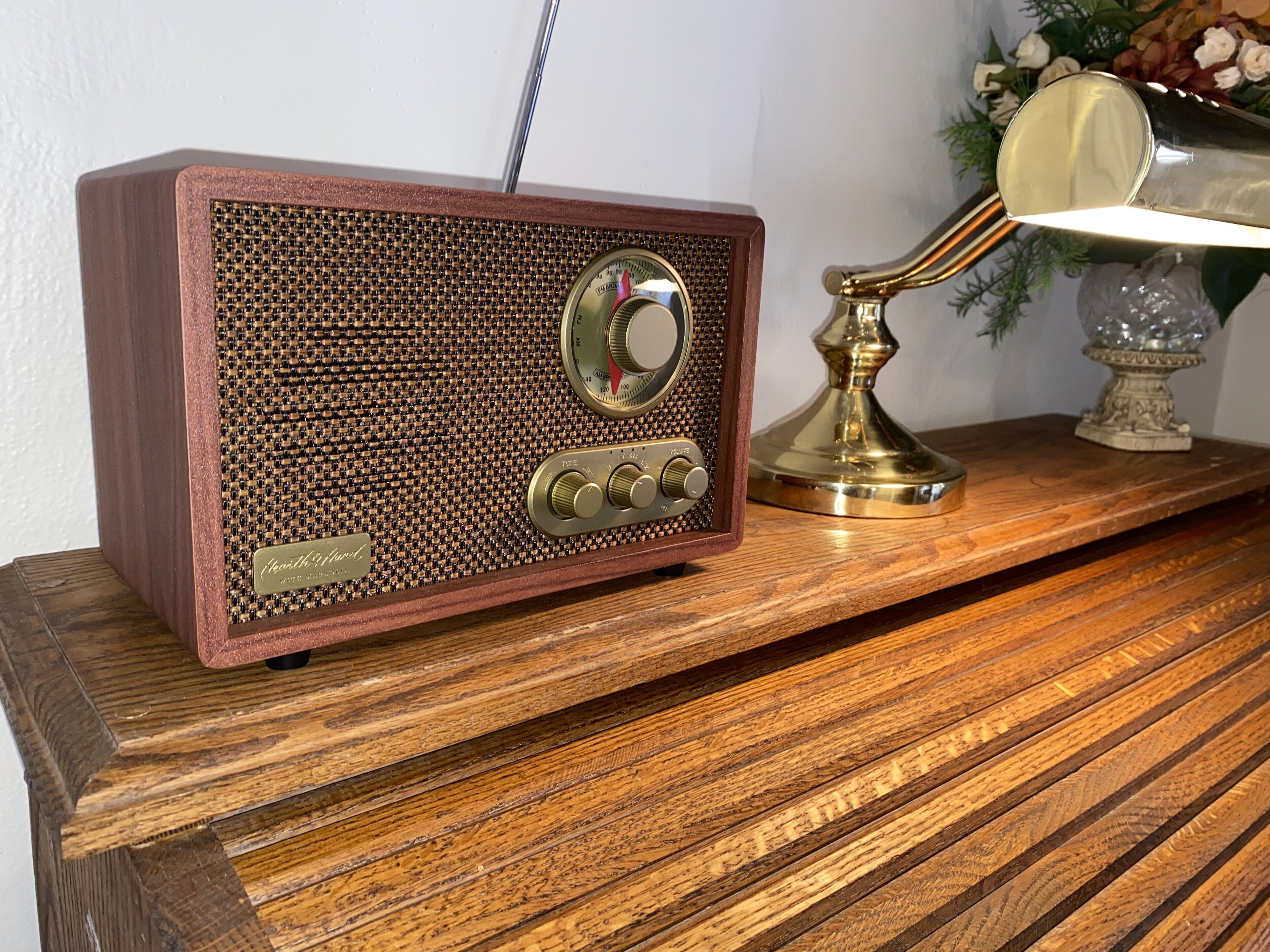 A vintage radio with a wooden frame and a brass speaker, placed on a wooden table next to a brass lamp.