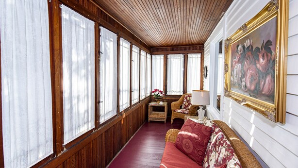 Une pièce avec un plancher en bois, un canapé rouge, une petite table avec une lampe et un tableau accroché au mur.