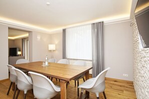 A hotel room with a wooden dining table, white chairs, a TV, a lamp, and a large window with curtains. - Ruhig und Idyllische Lage, Ahoi Erlebnisbad Gratis - Gutshaus Silvitz Fewo 01 - Gutshaus Silvitz (Bergen auf Rügen)