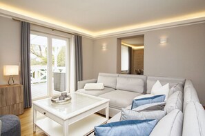 A modern living room with a white sofa, a glass coffee table, and a view of the outdoors. - Ruhig und Idyllische Lage, Ahoi Erlebnisbad Gratis - Gutshaus Silvitz Fewo 01 - Gutshaus Silvitz (Bergen auf Rügen)