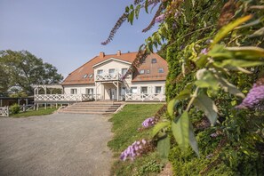 A two-story house with a balcony, a front entrance, and a paved driveway. - Ruhig und Idyllische Lage, Ahoi Erlebnisbad Gratis - Gutshaus Silvitz Fewo 01 - Gutshaus Silvitz (Bergen auf Rügen)