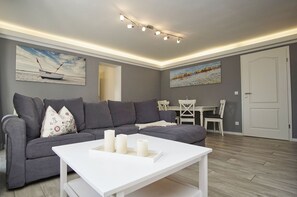 A modern living room with a grey sofa, white coffee table, and two paintings on the wall. - Ruhig und Idyllische Lage, Ahoi Erlebnisbad Gratis - Gutshaus Silvitz Fewo 02 - Gutshaus Silvitz (Bergen auf Rügen)