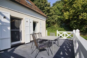 A wooden deck with a table and chairs, a white fence, and a building with white shutters.