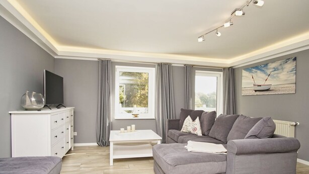 Una sala de estar moderna con un sofá gris, una mesa de centro blanca y un televisor de pantalla plana sobre un mueble blanco.