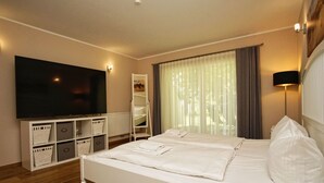 Una habitación de hotel con una cama grande, un televisor en la pared, un armario y una ventana con cortinas.
