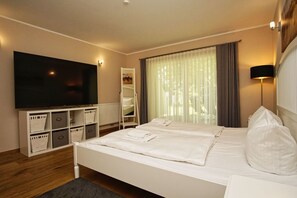 A hotel room with a large bed, a TV on the wall, a wardrobe, and a window with curtains.