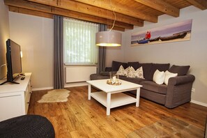 A cozy living room with a wooden ceiling, a white coffee table, a grey sofa, and a painting of a boat on the wall. - Ruhig und Idyllische Lage, Ahoi Erlebnisbad Gratis - Gutshaus Silvitz Fewo 03 - Gutshaus Silvitz (Bergen auf Rügen)