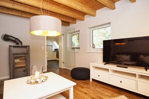 En moderne stue med træloft, hvidt tv-møbel, fladskærms-tv og brændeovn.