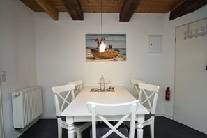 A dining area with a white table and chairs, a painting of a boat on the beach, a white radiator, and a fire extinguisher on the wall. - Ruhig und Idyllische Lage, Ahoi Erlebnisbad Gratis - Gutshaus Silvitz Fewo 03 - Gutshaus Silvitz (Bergen auf Rügen)