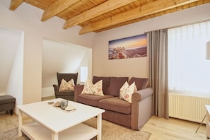 A cozy living room with a brown sofa, a white coffee table, and a painting of a beach scene on the wall. - Ruhig und Idyllische Lage, Ahoi Erlebnisbad Gratis - Gutshaus Silvitz Fewo 04 - Gutshaus Silvitz (Bergen auf Rügen)
