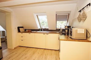 A compact kitchen with wooden cabinets, a countertop, a coffee maker, and a window with a view of trees. - Ruhig und Idyllische Lage, Ahoi Erlebnisbad Gratis - Gutshaus Silvitz Fewo 04 - Gutshaus Silvitz (Bergen auf Rügen)
