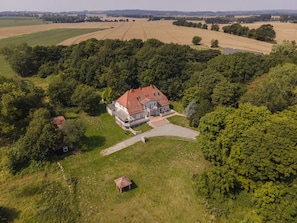 A large house with a red roof surrounded by lush greenery and fields. - Ruhig und Idyllische Lage, Ahoi Erlebnisbad Gratis - Gutshaus Silvitz Fewo 04 - Gutshaus Silvitz (Bergen auf Rügen)
