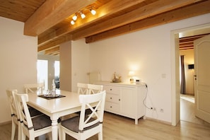 Een eetruimte met een witte tafel en stoelen, een wit kastje en een plafond met zichtbare houten balken.