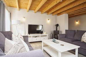 Un salon moderne avec un plafond en bois, un téléviseur à écran plat, des canapés gris, une table basse blanche et une cheminée.