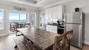 A spacious kitchen with white cabinets, a stainless steel refrigerator, and a wooden dining table. - Isle Oasis. Oceanfront. Elevator, Heatable Pool,  Drct Bch Access. Grt Location. (Holden Beach)