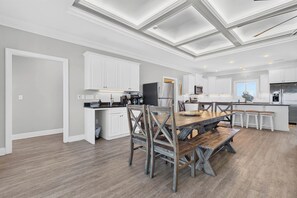 A modern kitchen with white cabinetry, a wooden dining table, and a breakfast bar. - Isle Oasis. Oceanfront. Elevator, Heatable Pool,  Drct Bch Access. Grt Location. (Holden Beach)