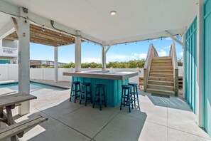 Un espace extérieur abrité comprenant une piscine, un bar avec des tabourets et un escalier en bois.